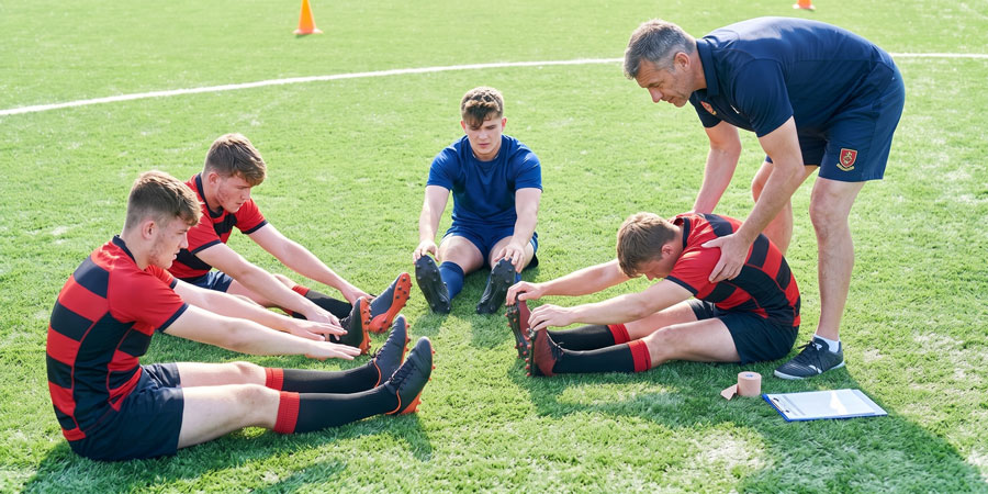 coach assists kids stretching on green turf field Teenage Rugby Players Stretching